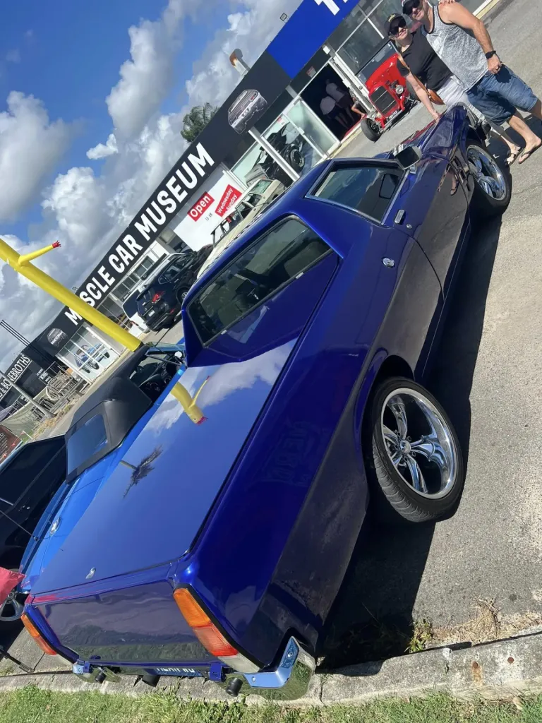 Dark blue classic ute with chrome wheels parked outside the Muscle Car Museum, two people standing behind