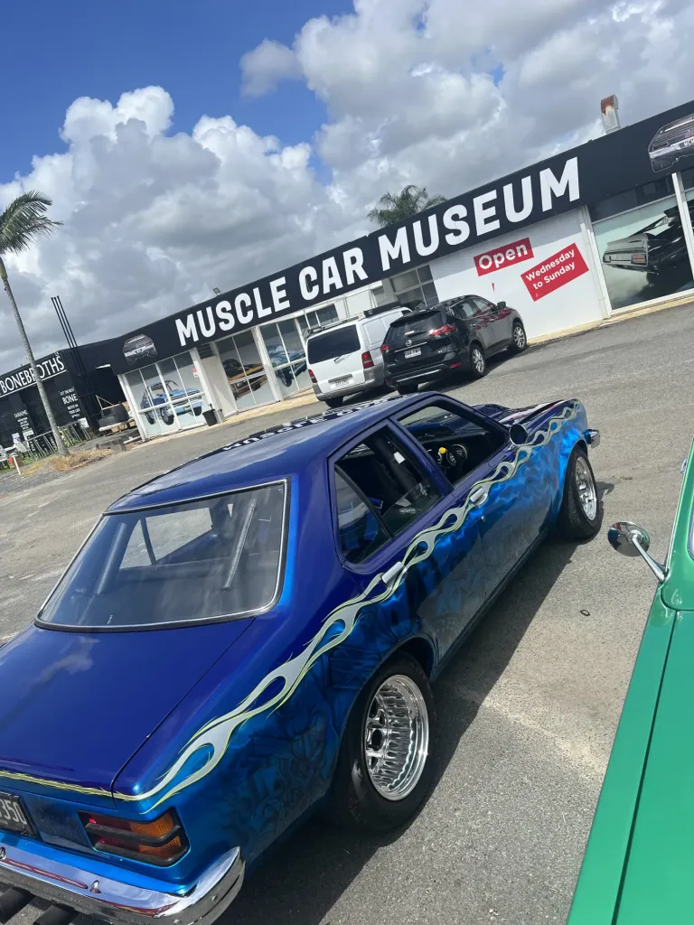 Blue classic sedan with silver flame paintwork parked outside the Muscle Car Museum