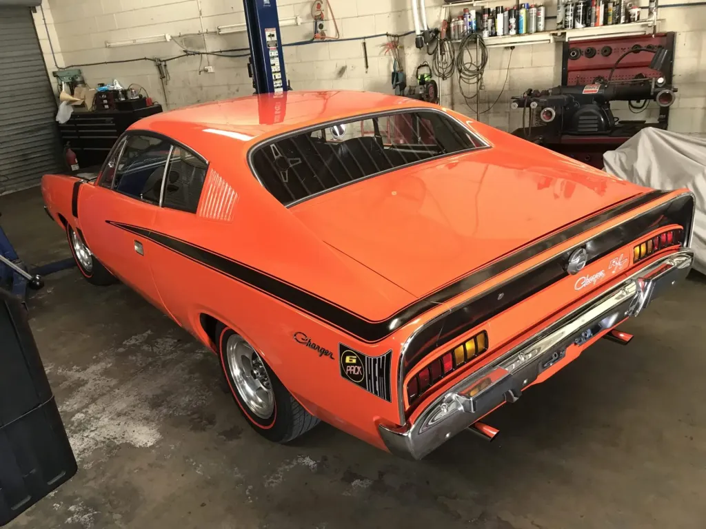 Rear three-quarter view of an orange Chrysler Valiant Charger R/T with black stripes in a workshop