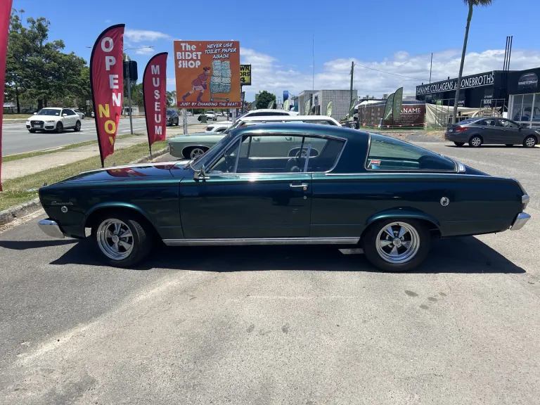 Side view of a dark green 1960s fastback coupe parked near the museum's Open flag banners