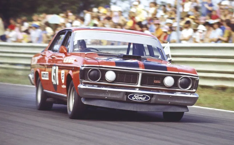 Red and blue Ford Falcon XY GT race car cornering on a circuit in front of a crowd of spectators