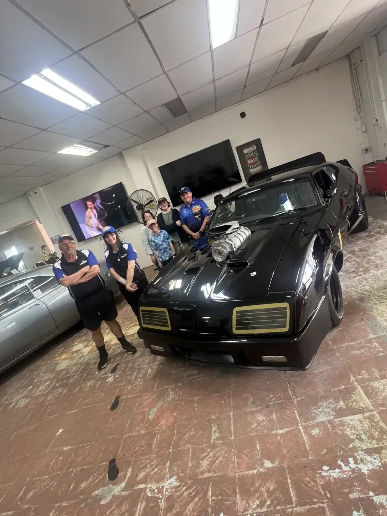 Group of six people posing in the showroom beside the black Interceptor replica with supercharger