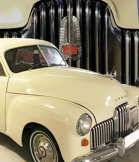 Cream Holden FX sedan in front of a large chrome Holden grille display