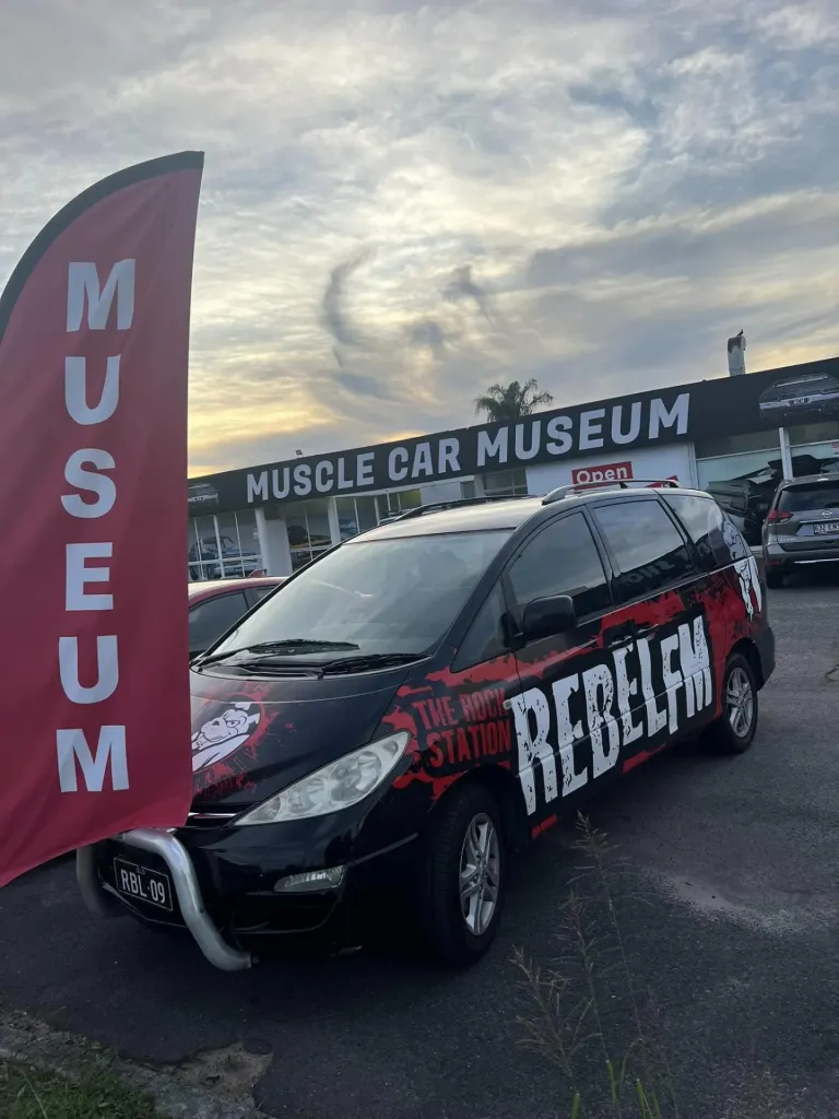 Black van in Rebel FM radio livery parked outside the Muscle Car Museum at dusk