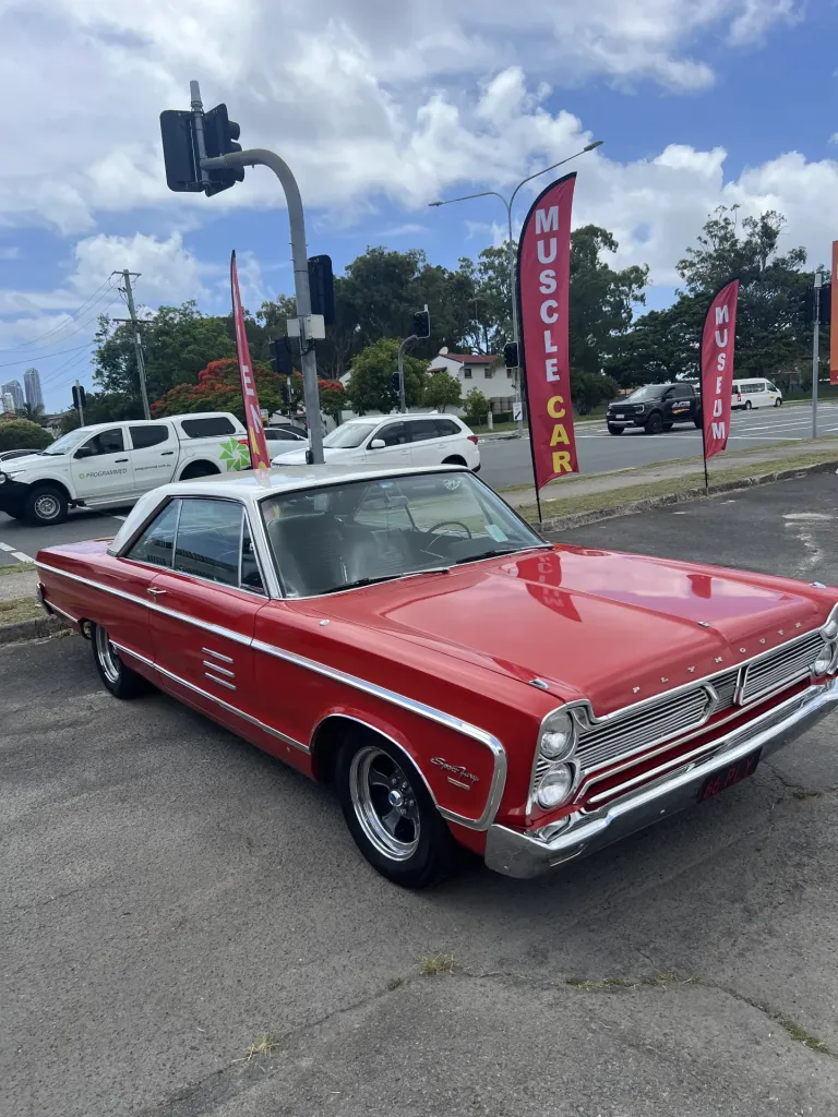 Red 1960s American hardtop with chrome side trim parked beside Muscle Car Museum flag banners