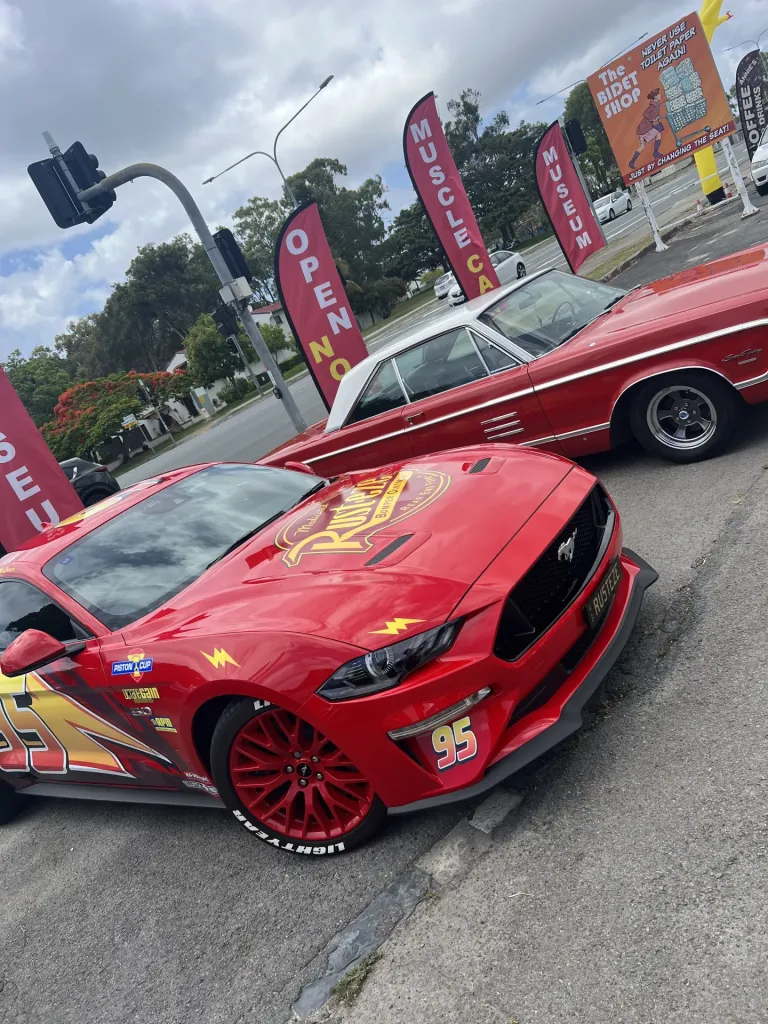 Red modern Ford Mustang in Lightning McQueen number 95 livery parked beside a red classic hardtop