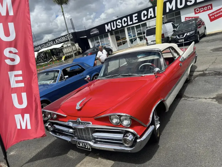 Red and white 1950s American hardtop with chrome grille and tail fins at a car meet outside the museum