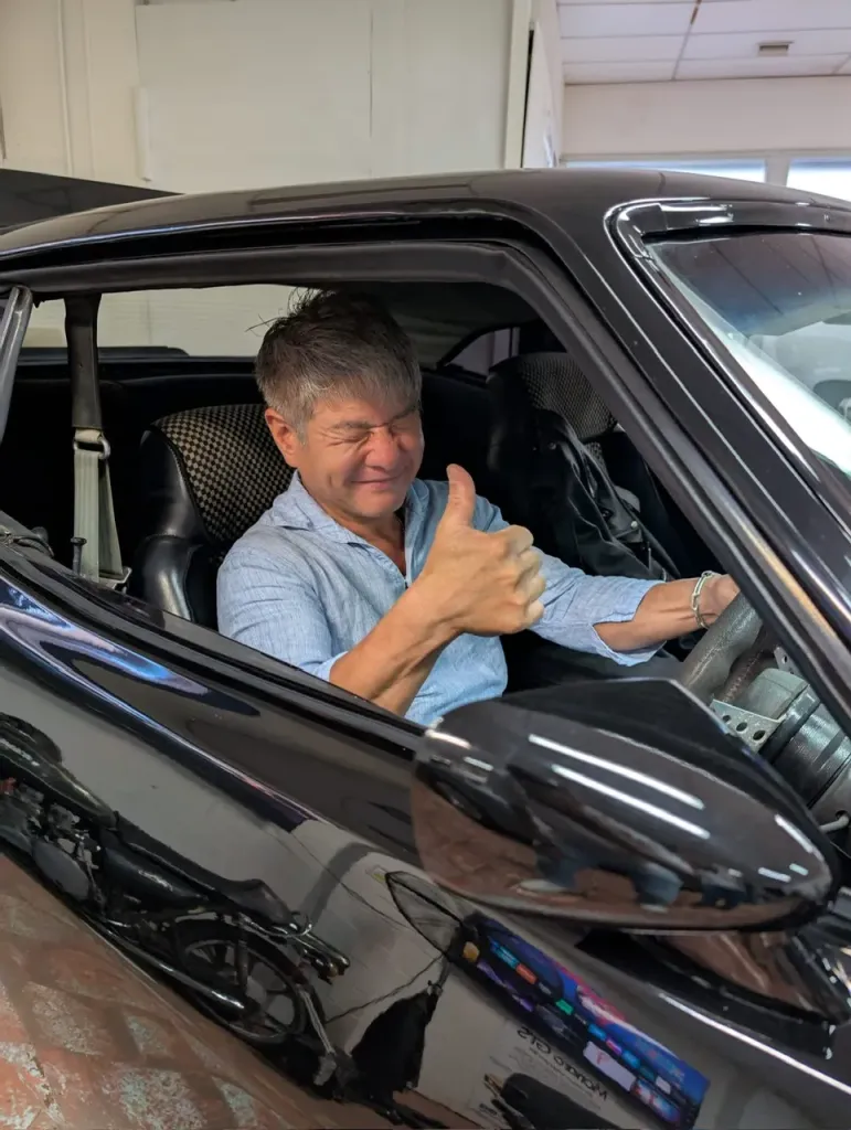 Smiling man giving a thumbs up from the driver's seat of a black car
