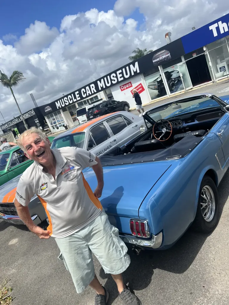 Smiling man beside a light blue classic convertible at a car meet outside the museum