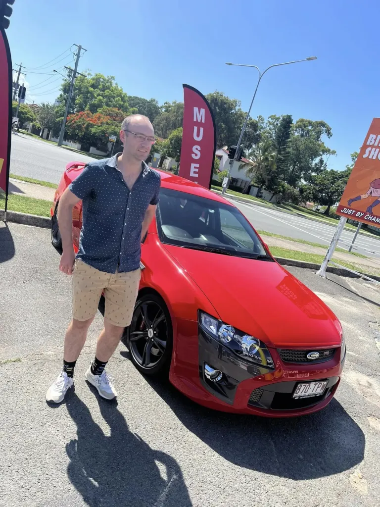Man in a navy shirt standing beside a red modern Ford performance sedan in the car park