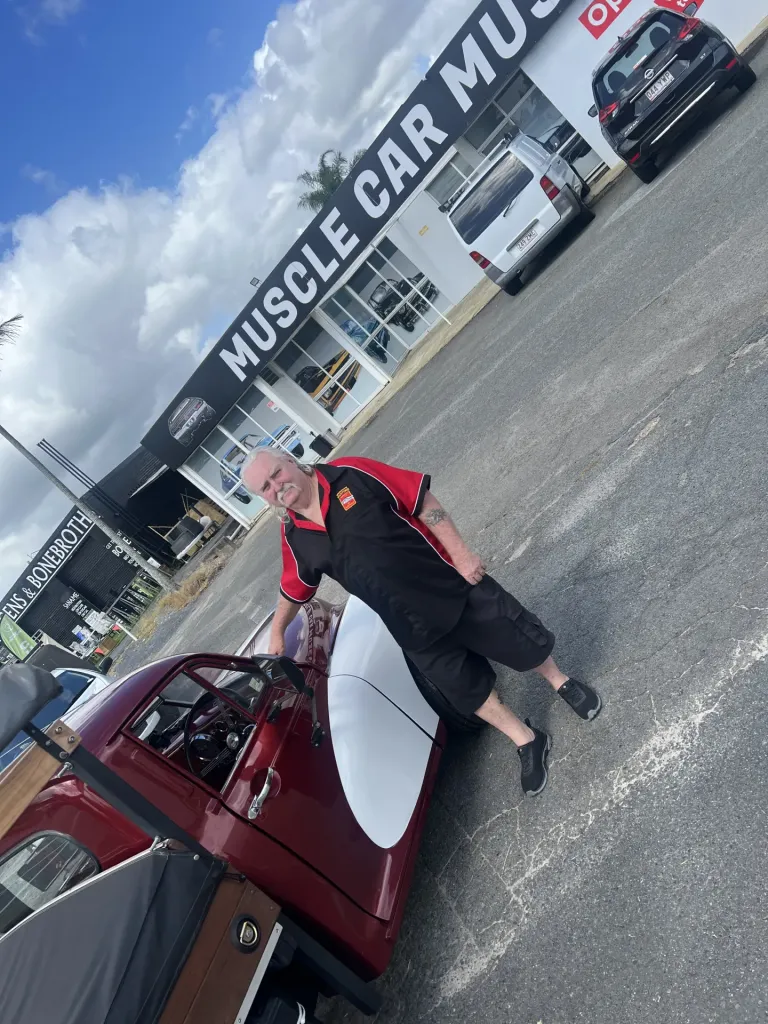 Man in a black and red shirt standing beside a red ute in front of the Muscle Car Museum