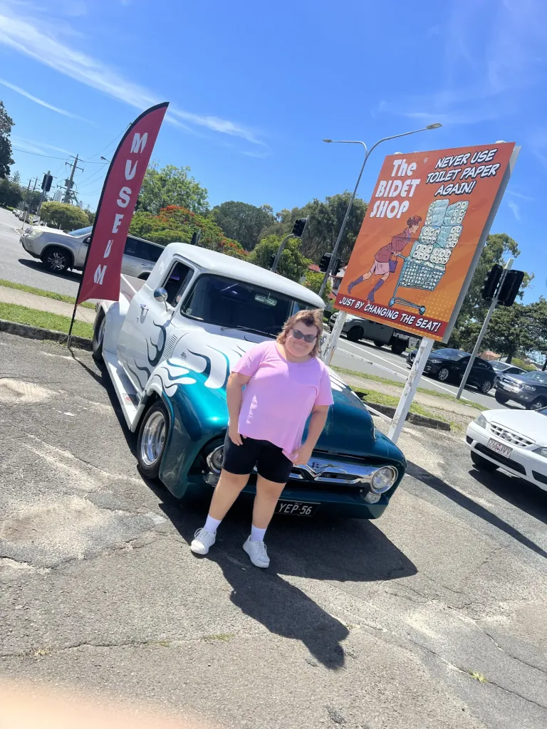 Woman in a pink top posing in front of a teal 1950s pickup truck with white flame paint