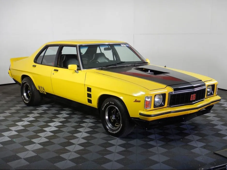 Yellow Holden Monaro GTS four-door sedan with a black bonnet stripe and scoop on a chequered floor